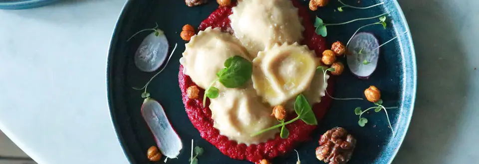 Plate of tasty ravioli with beet sauce served on plate with nuts and herbs