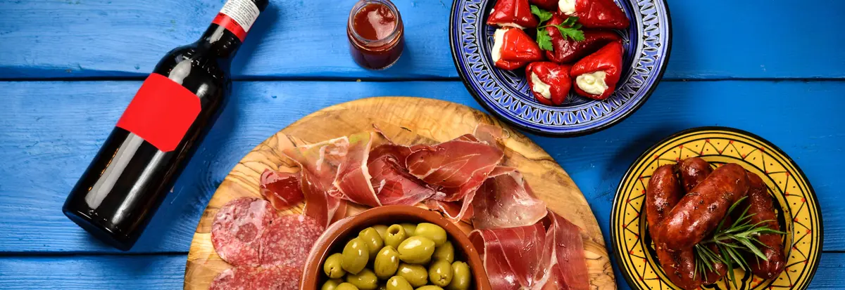 Plats of tapas and a bottle of wine on a bright blue wooden table.
