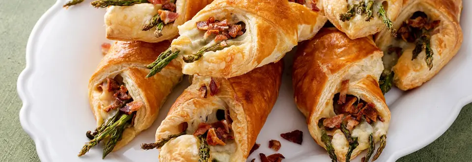 Asparagus appetizers wrapped in puff pastry with melted cheese and topped with bacon