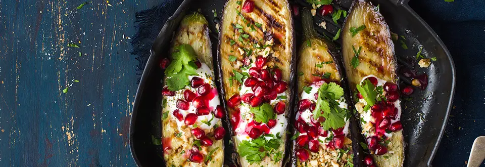 A platter of slices of grilled eggplants with garlic yogurt sauce, walnuts and pomegranate, top view