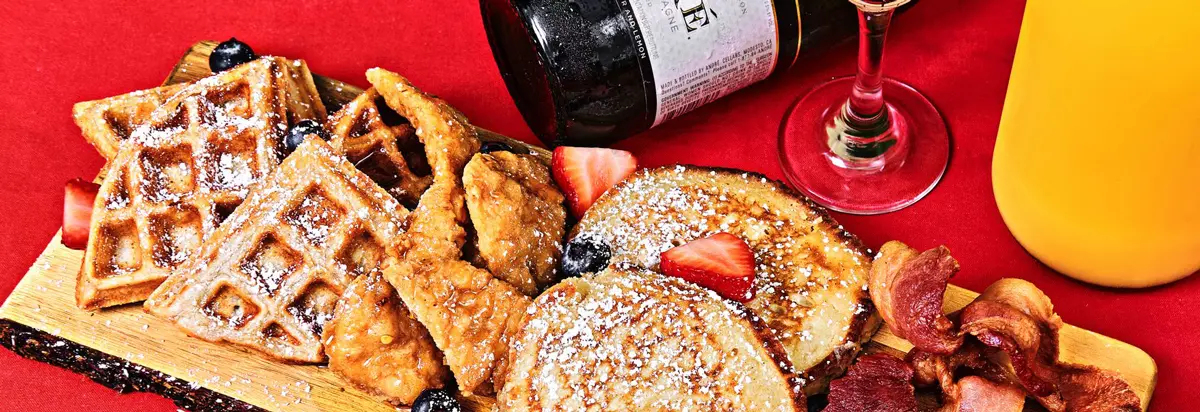 A vibrant breakfast setup with pancakes, waffles, bacon, and fresh fruit on a wooden tray.