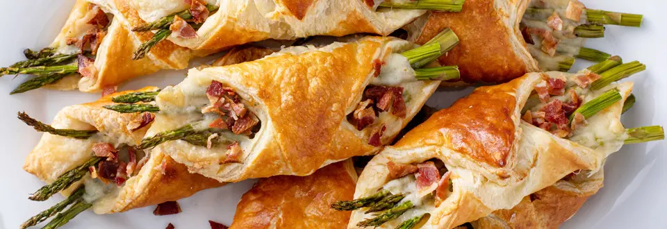 Asparagus appetizers wrapped in puff pastry with melted cheese and topped with bacon