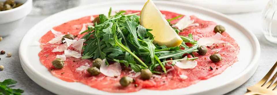 Beef carpaccio with capers, arugula and parmesan on a white plate, selective focus.