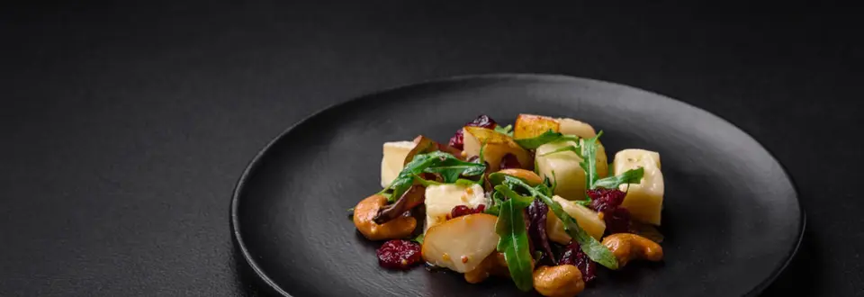 Delicious fresh vegan salad with pear, brie cheese, nuts and grains, and arugula on a ceramic plate on a dark background