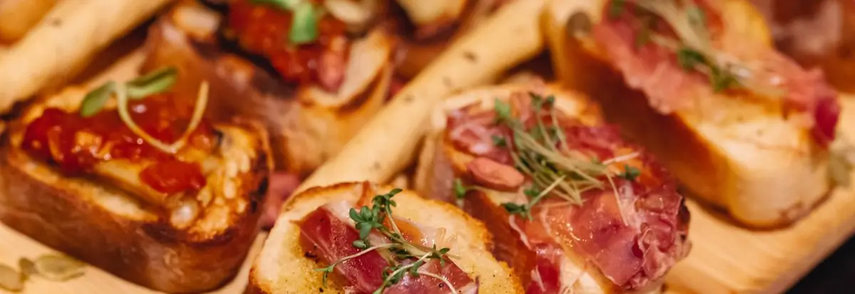 Delicious bruschetta with prosciutto and herbs served on a rustic wooden board.