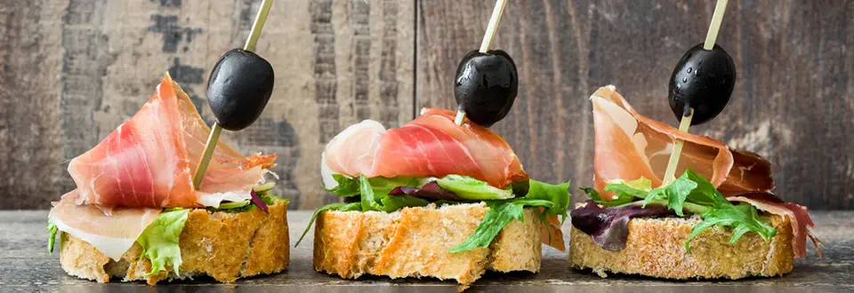 Spanish serrano ham skewers with olives and lettuce on a rustic wooden background.
