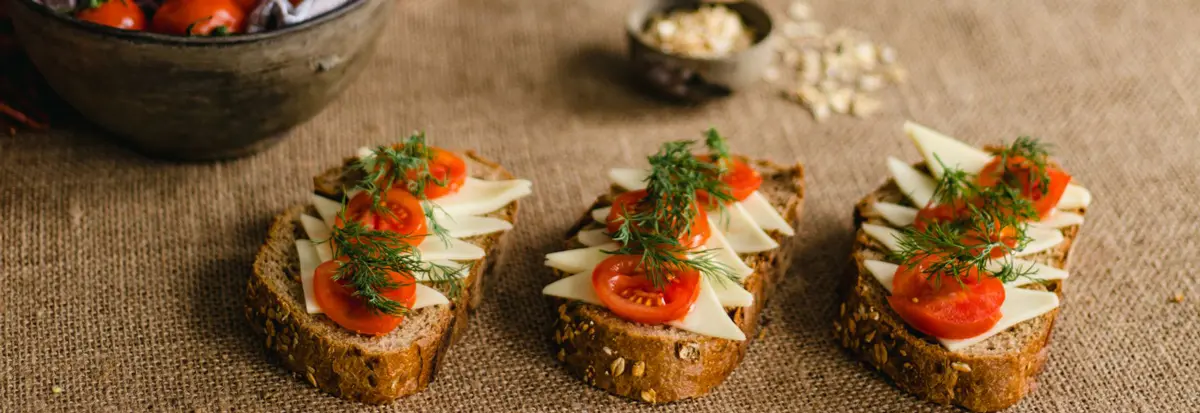 Rustic multigrain bread topped with cheese, tomatoes, and dill on a burlap surface