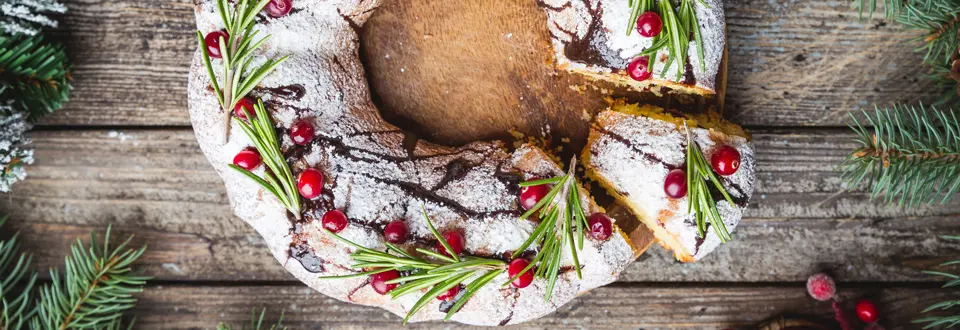 Traditional homemade christmas cake holiday dessert with cranberry and chocolate with new year tree decoration on vintage wooden table background.